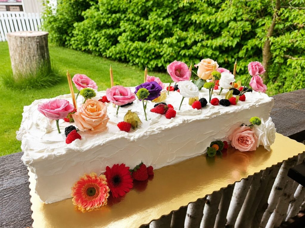 Tort dreptunghiular cu glazură albă, decorat cu trandafiri, flori naturale colorate și fructe de pădure proaspete